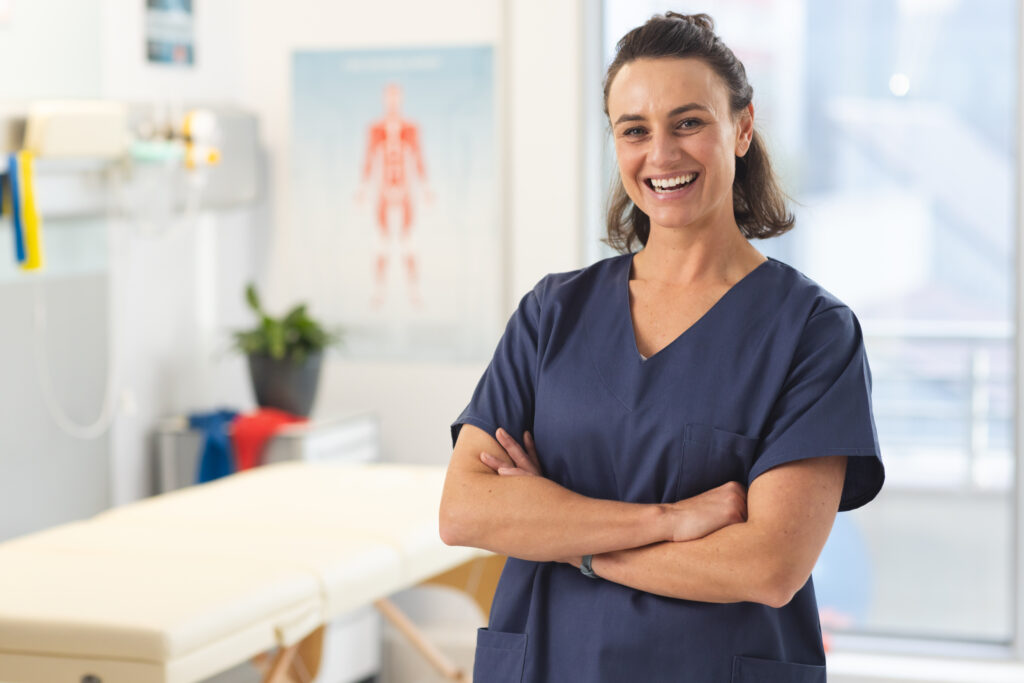 Portrait of happy female caucasian physiotherapist wearing scrubs at hospital. Hospital, physiotherapy, work, medicine and healthcare, unaltered.